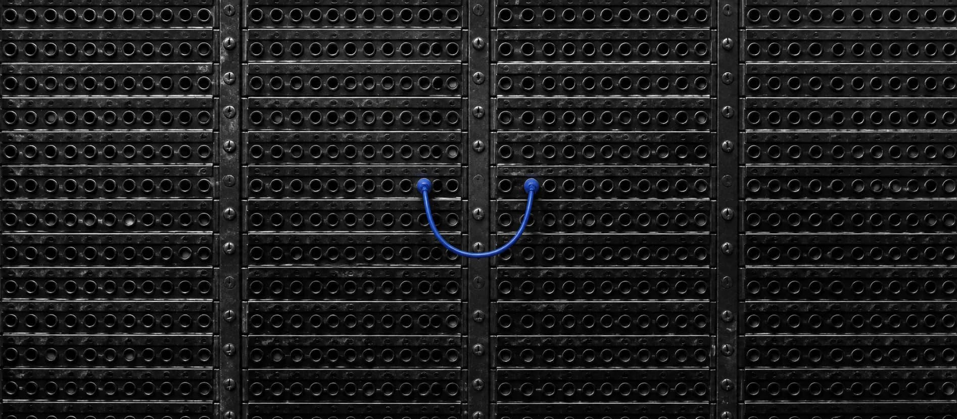 A single cobalt patch cord connects two ports on a dark analog telephone exchange.